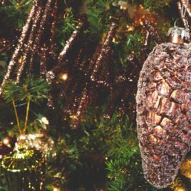 Brown-colored glittered pinecone Christmas ornament hanging on a tree branch for the perfect Christmas tree.