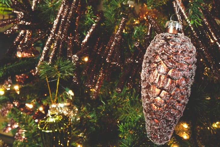 Brown-colored glittered pinecone Christmas ornament hanging on a tree branch for the perfect Christmas tree.