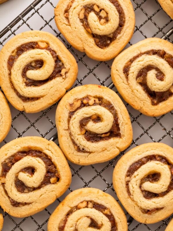 Top down view of golden cookies filled with dates and nuts and rolled in a circle sitting on a cooling rack