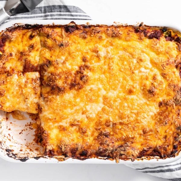 Top down view of white pan holding cheese covered lasagna with rag underneath