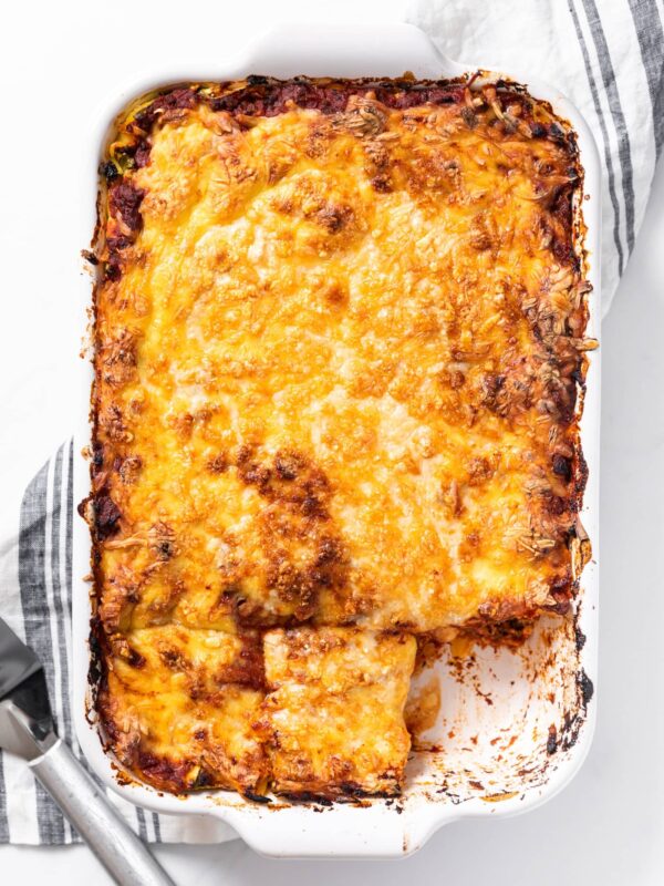 Top down view of large white pan filled with homemade lasagna with golden cheese on top and one piece missing