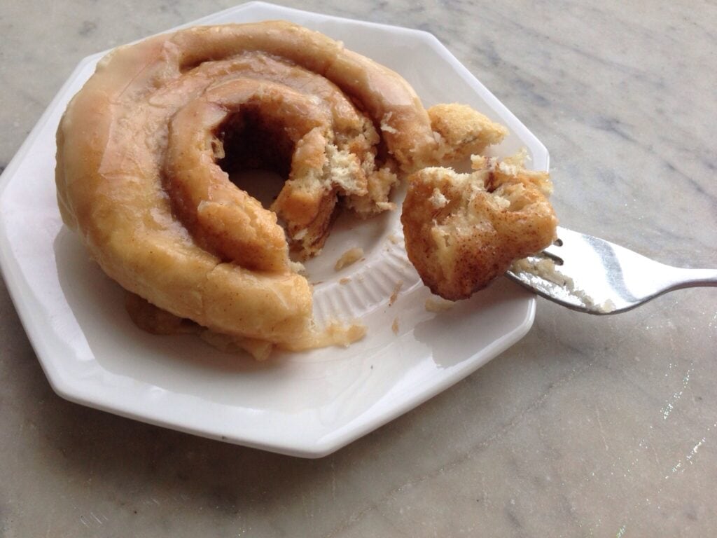 White plate with bite removed from a cinnamon roll with brown butter frosting.