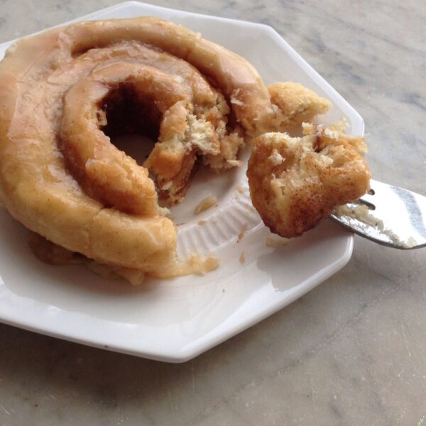 White plate with bite removed from a cinnamon roll with brown butter frosting.