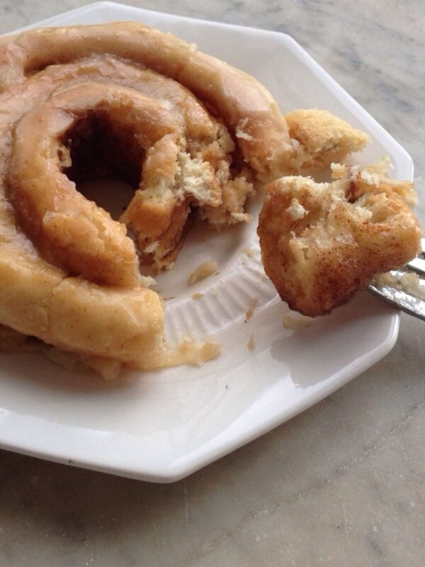 White plate with bite removed from a cinnamon roll with brown butter frosting.