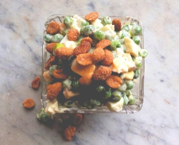 Square glass dish sitting on marble countertop filled with spring salad made from peas and eggs and topped with peanuts and cheese