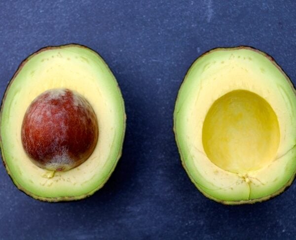 Two avocados one with a pit and the other without sitting on blue surface