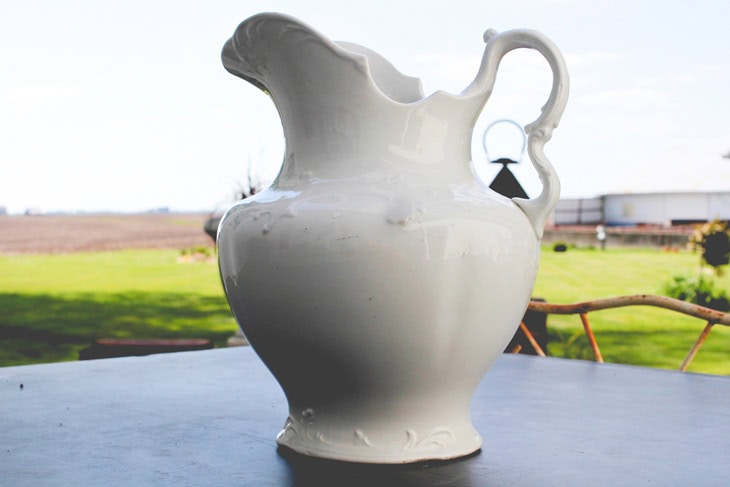 Large white ironstone container sitting on a slate table in a garden before being filled with flowers.