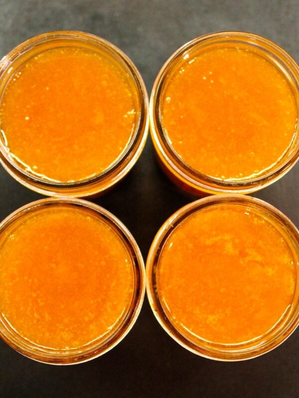 Top down view of orange-colored apricot butter in glass jars sitting on a black surface