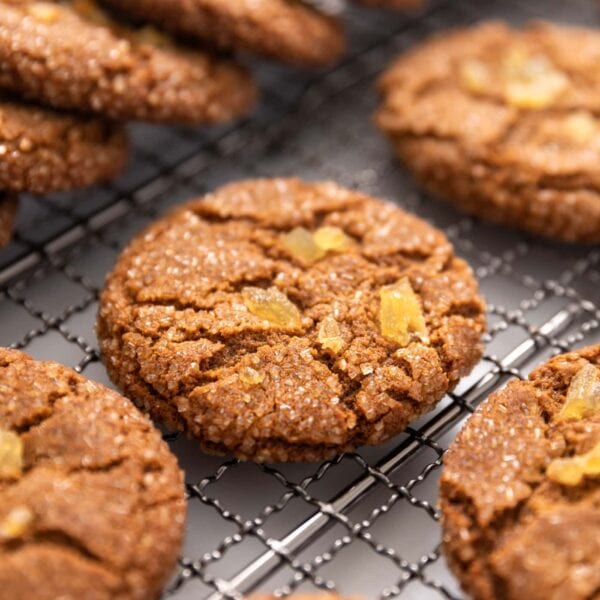Brown colored molasses crinkle cookie sitting on cooling rack with other cookies stacked around