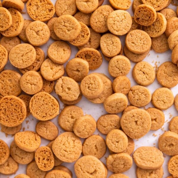 Top down view of small golden peppernuts sitting on white piece of parchment after coming out of the oven