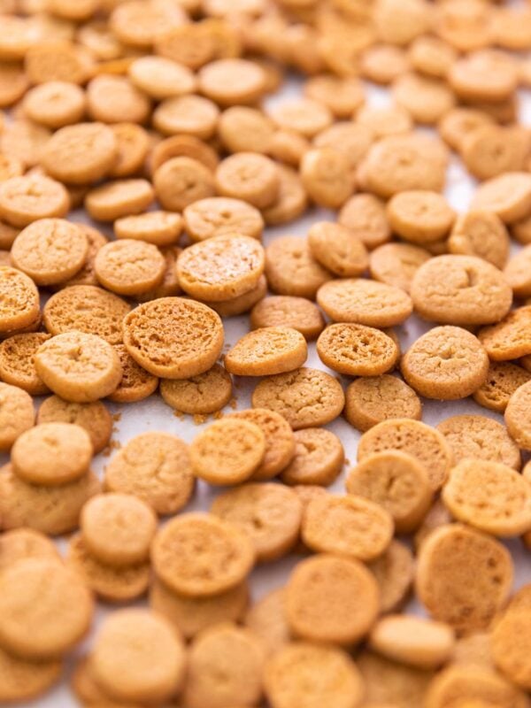 Small golden peppernuts sitting on white piece of parchment cooling after being in the oven