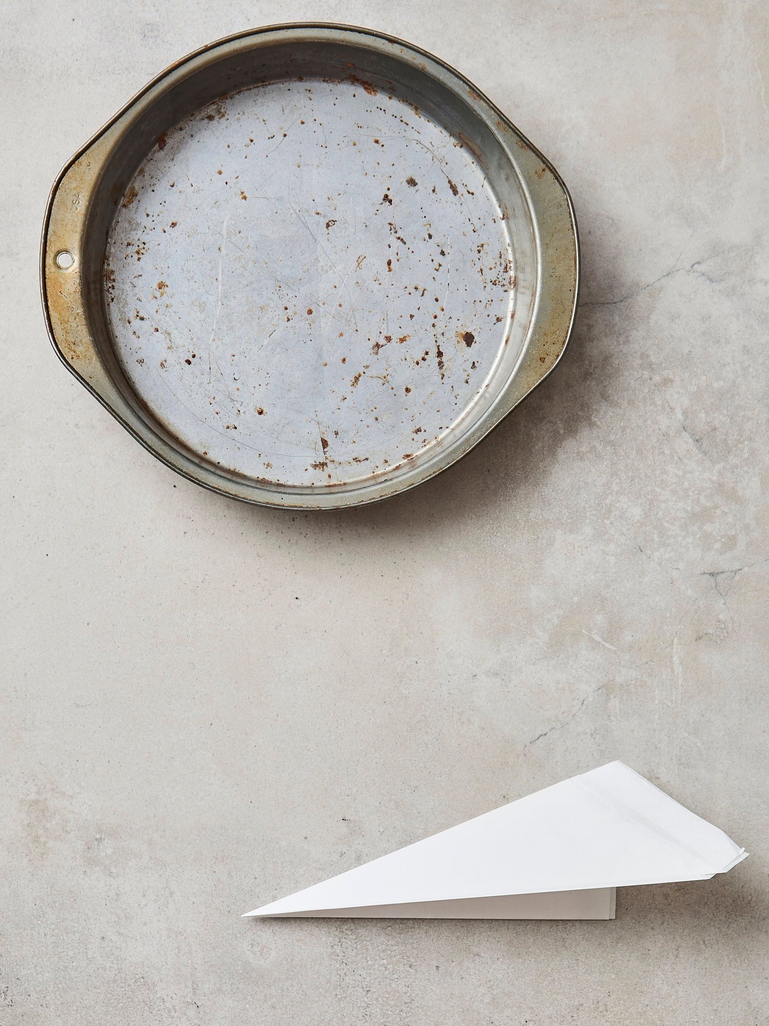 Cake pan with triangle of parchment folded showing how to fold it.