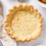White surface with baked golden brown pie crust with dock marks on the bottom cooling after coming out of the oven.