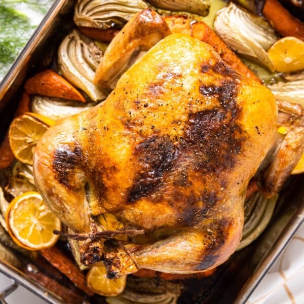 Top down view of metal baking pan filled with roasted chicken sitting on top of roasted vegetables with white kitchen towel underneath