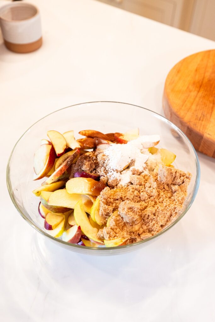 Glass bowl filled with unmixed combination of apples, cinnamon, and sugar.