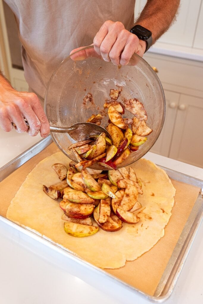 Pouring apple mixture on top of crust for an apple galette.
