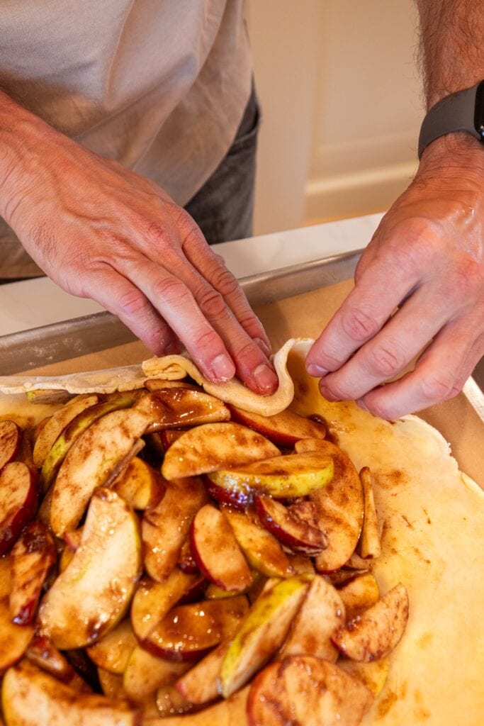Hand folding creases in dough for an apple galette.