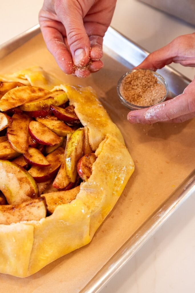 Sprinkling turbinado sugar on crust of pie dough for an apple galette.