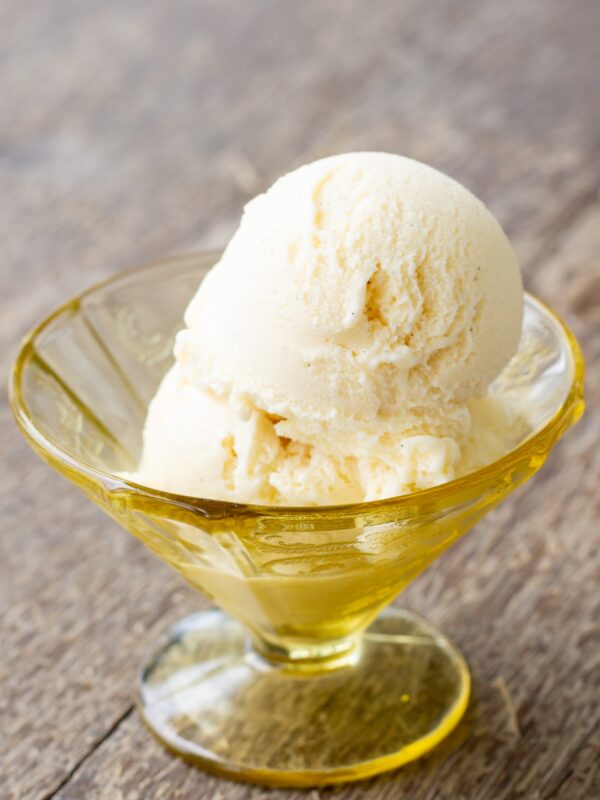 A scoop of vanilla ice cream sits in a glass dish.