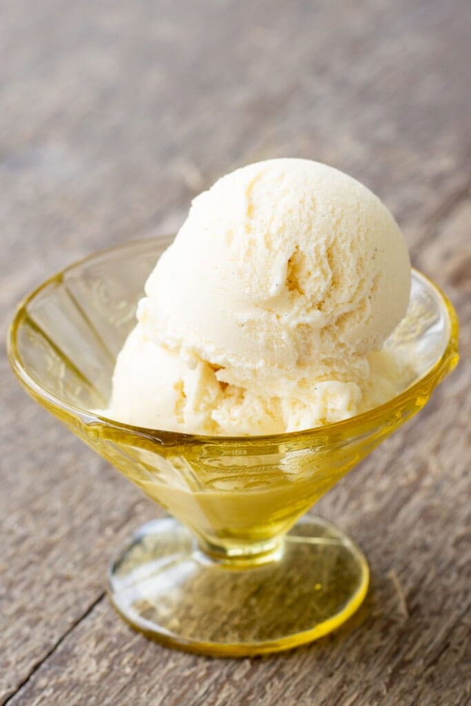 A scoop of vanilla ice cream sits in a glass dish.