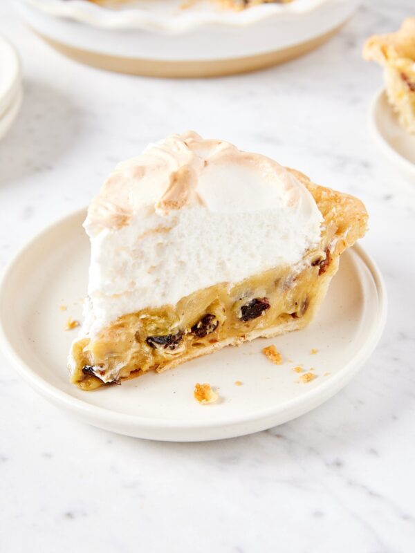 White plate with slice of sour cream raisin pie showing raisins inside and meringue topping.