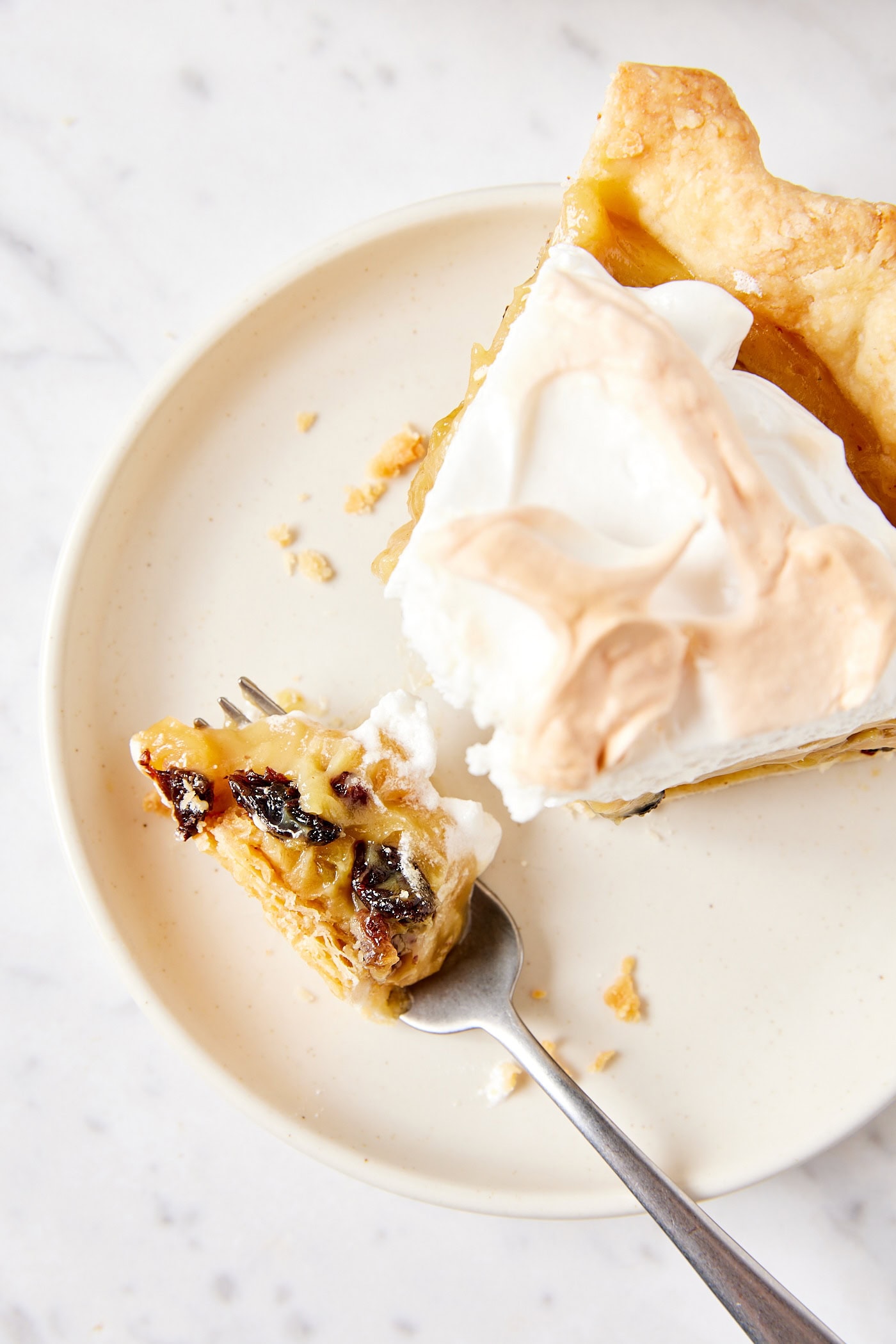 White plate with slice of sour cream raisin pie with fork scooping up a serving with raisins on it.