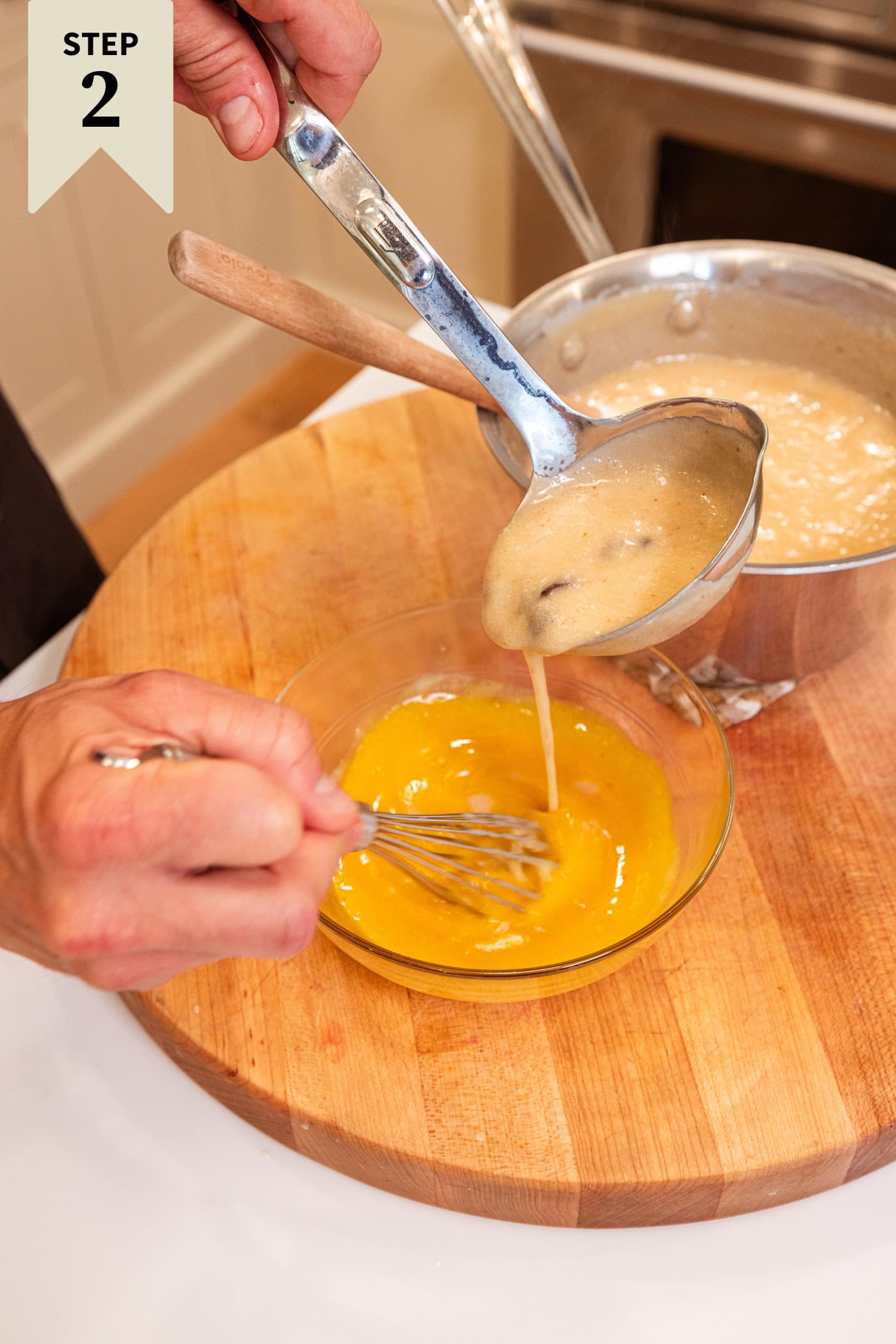 Hand using ladle to temper egg yolks with raisin pie custard filling.