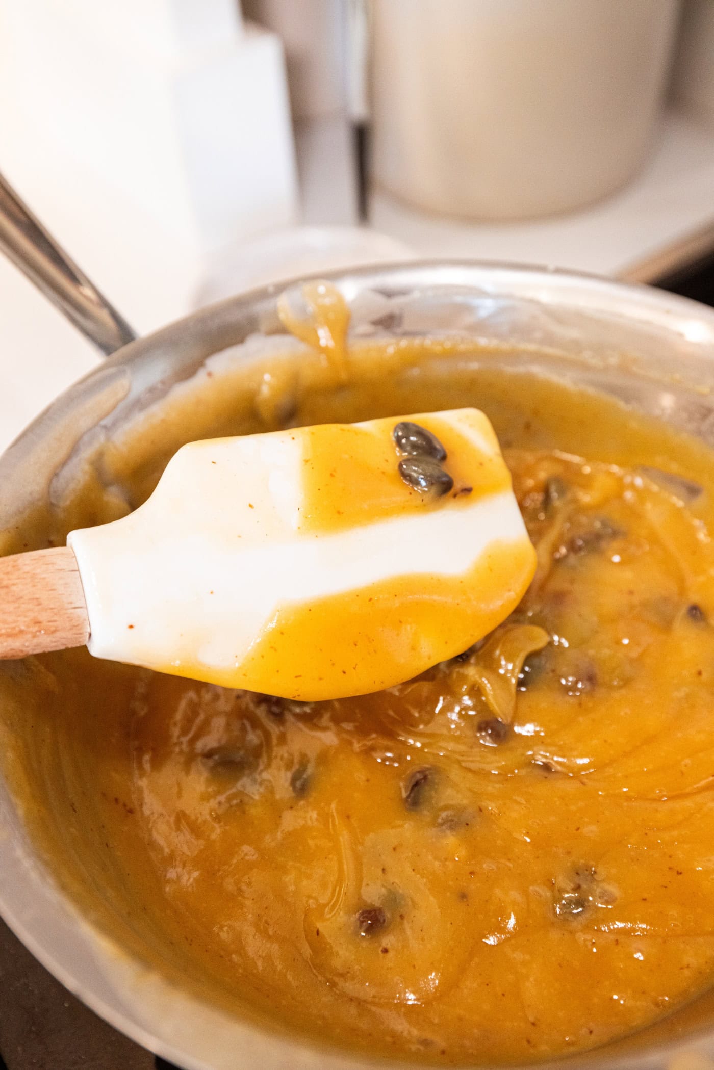 Spatula being held above sour cream raisin pie filling with a finger drawn through to show thick texture.