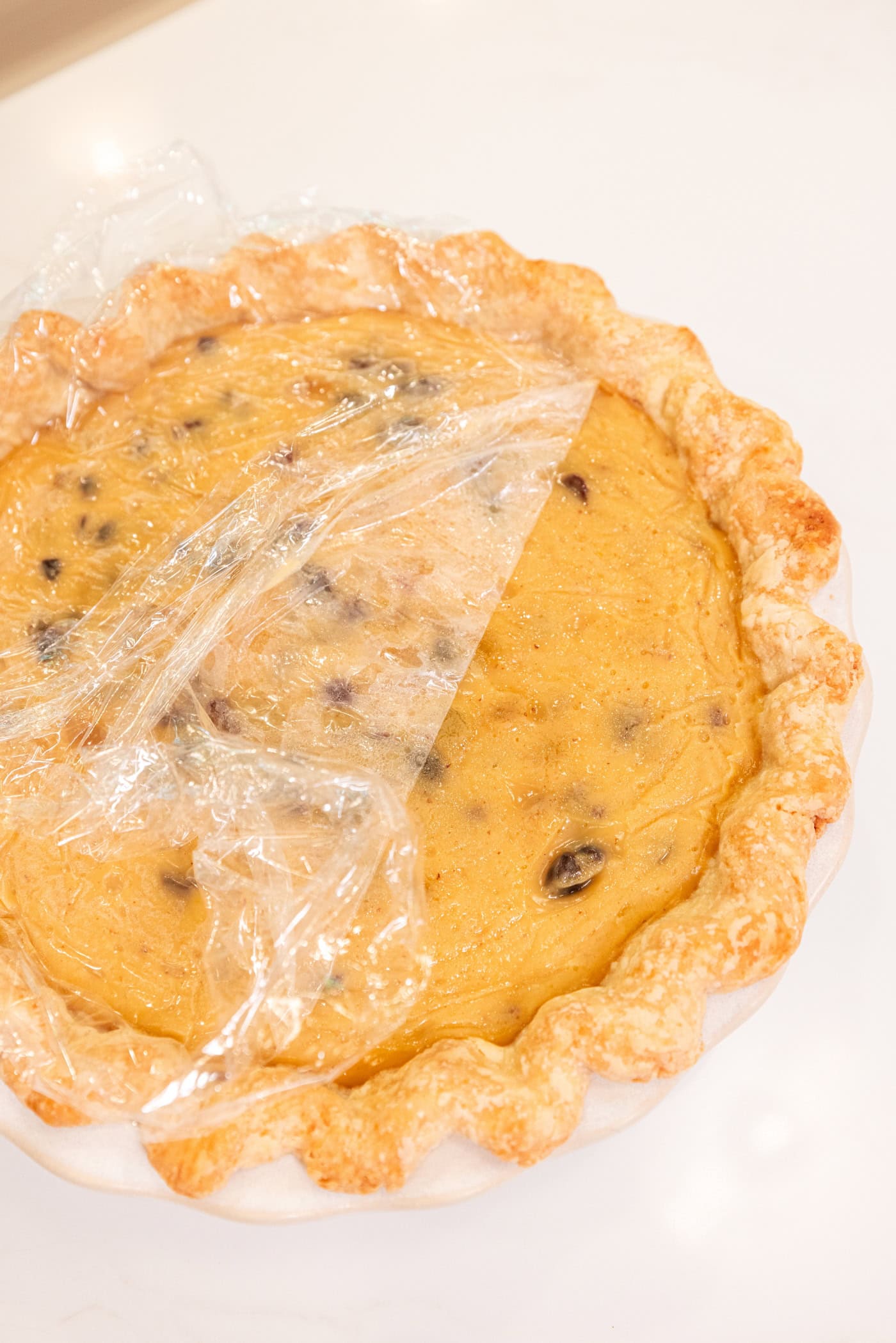 White surface with pie with custard filling with piece of plastic wrap on top to prevent a skin.