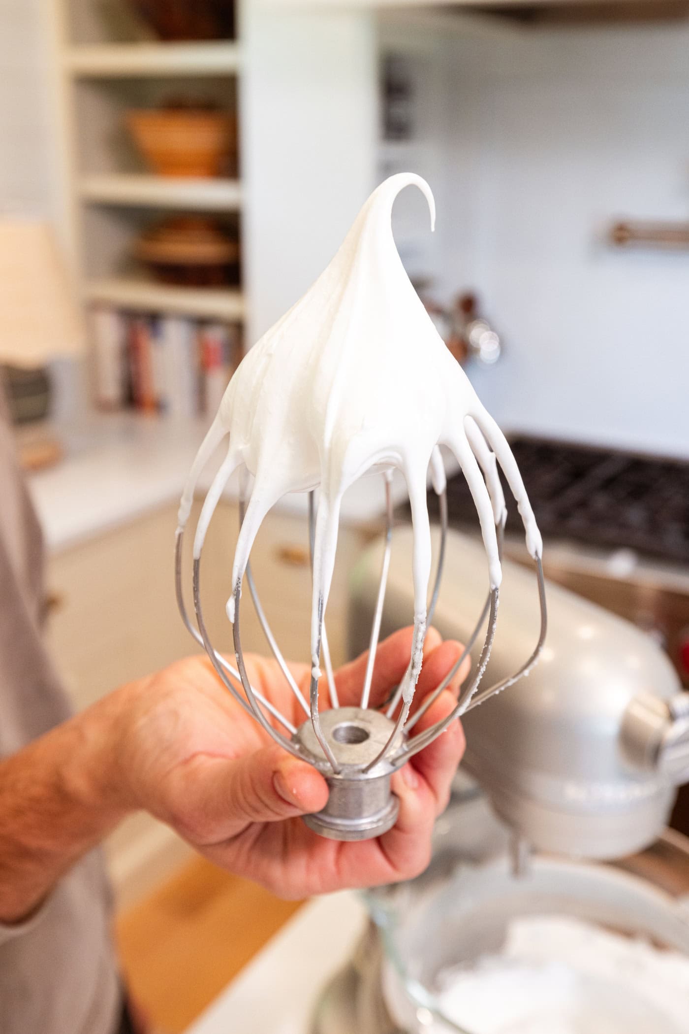 Hand holding whisk upside down with whipped meringue to show the texture.