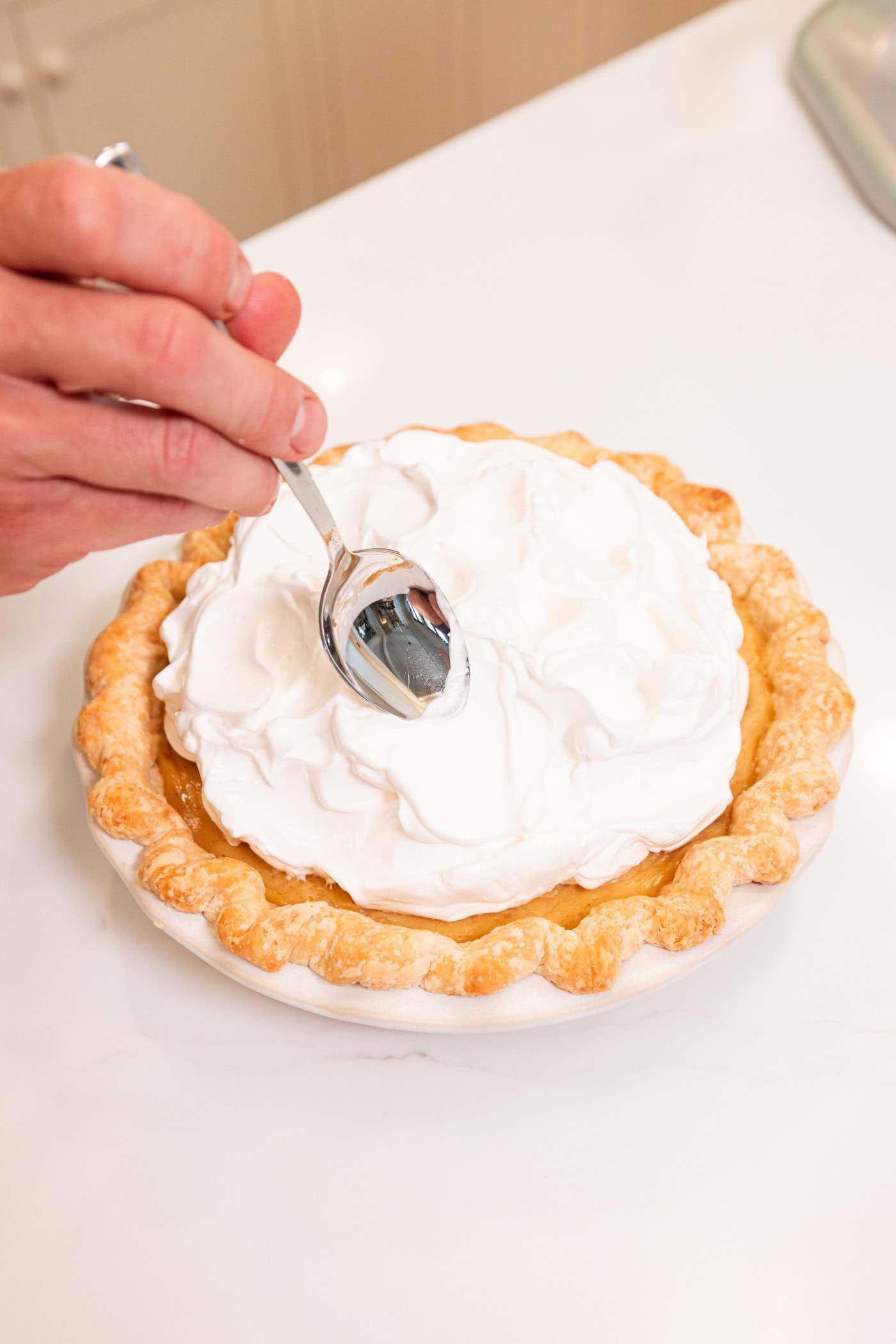 Hand using a spoon to create swoops in a meringue topping for a pie.