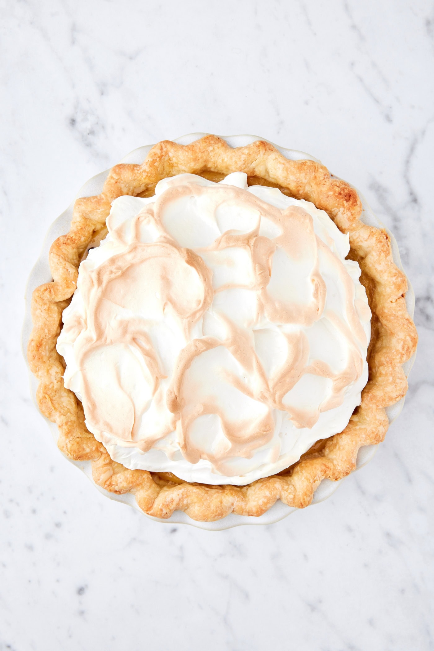 White marble surface with browned meringue topping on top of a pie.