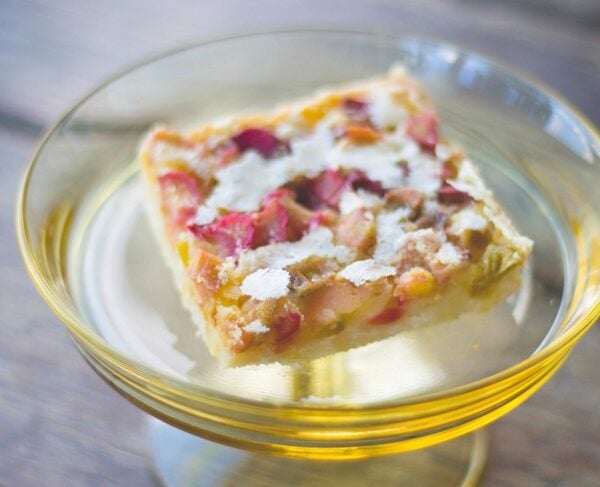 Yellow plate sitting on wood surface with square rhubarb bar sitting on plate showing red rhubarb pieces