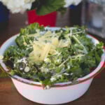 Large metal serving bowl filled with spicy pear kale salad sitting on outdoor summer table.