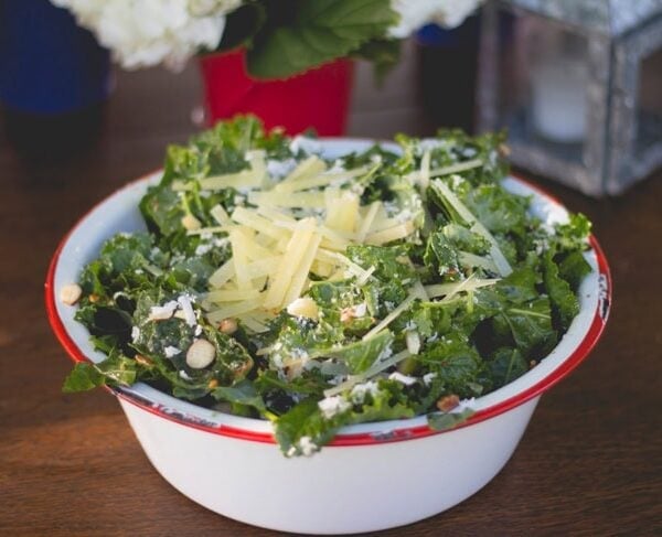 Large metal serving bowl filled with spicy pear kale salad sitting on outdoor summer table.