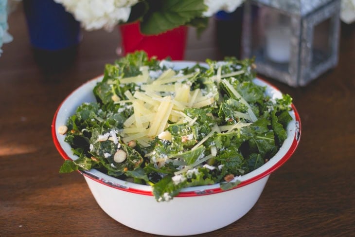 Large metal serving bowl filled with spicy pear kale salad sitting on outdoor summer table.
