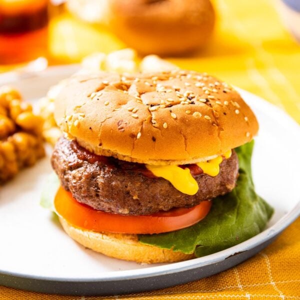 Grilled burger sitting on white plate with mustard running down side of patty with tomato and lettuce with baked beans on plate