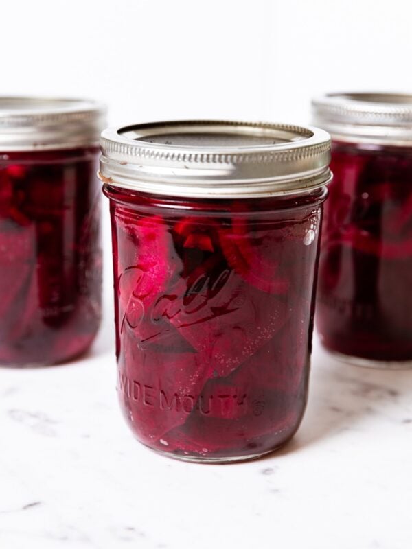 White marble surface with three jars filled with pickled beets in red liquid with lids and rings.