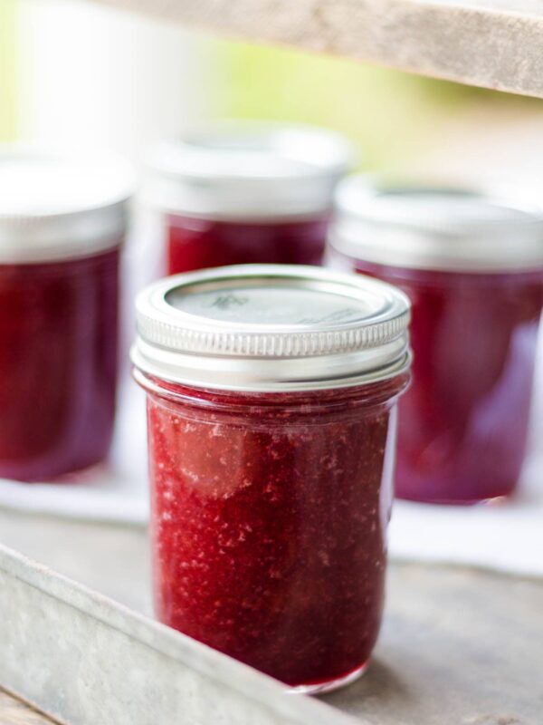 Jar of rhubarb butter on a silver metal tray with extra jars of rhubarb butter in background with white towel underneath