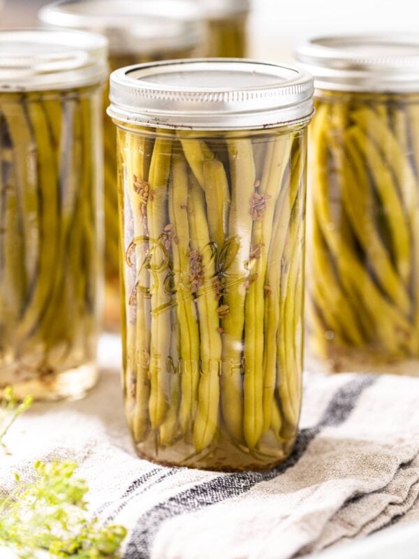 Glass jar sitting on towel filled with green beans and vinegar brine with other jars in background
