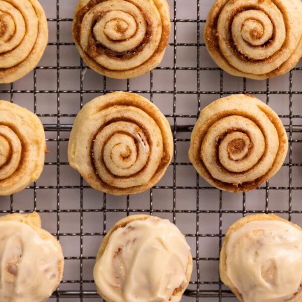 Top down view of little cinnamon roll cookie swirls some with white frosting all sitting on wire cooling rack