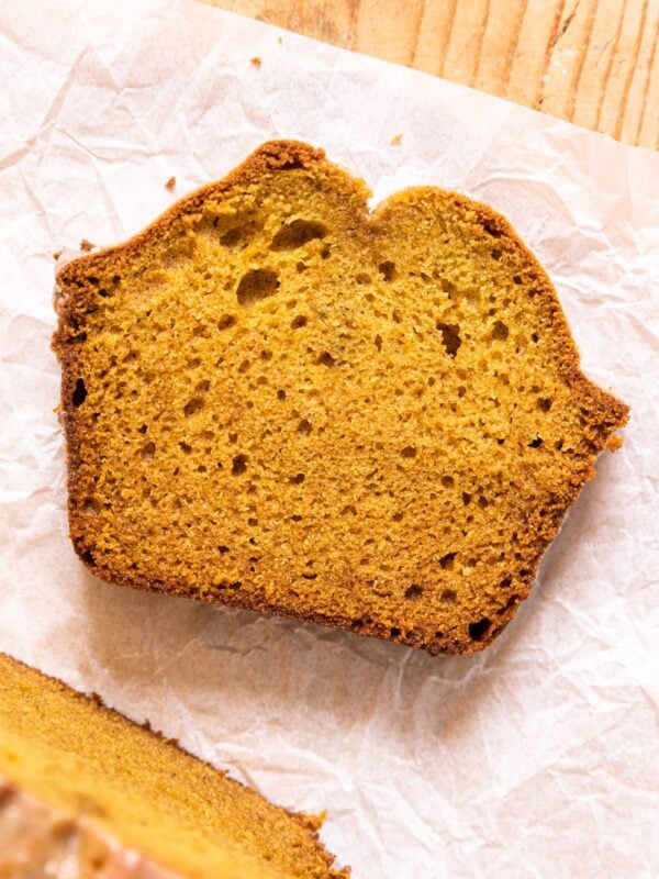Top down image of slice of pumpkin loaf sitting on crumpled piece of parchment on wood board