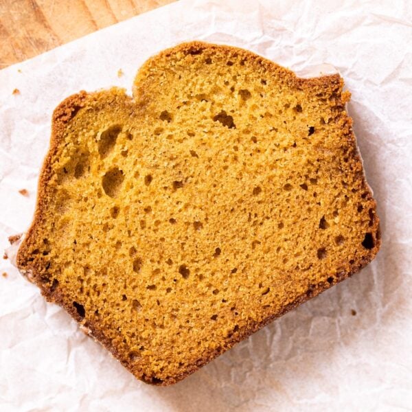 Top down view of slice of pumpkin loaf sitting on white piece of parchment paper on wood board