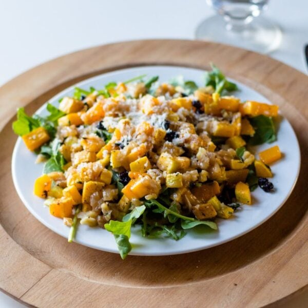 Butternut squash salad on a white plate with brown surface and silverware all on white surface
