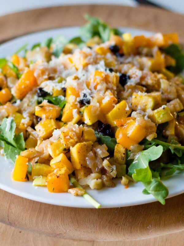 Butternut squash salad on a white plate with brown surface and silverware all on white surface