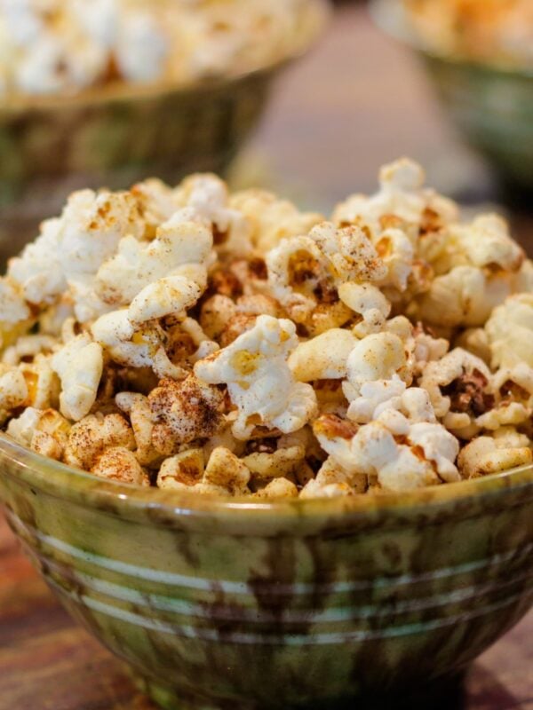 Green speckled bowl full of kettle corn sitting on wood surface with two bowls full of popcorn in background