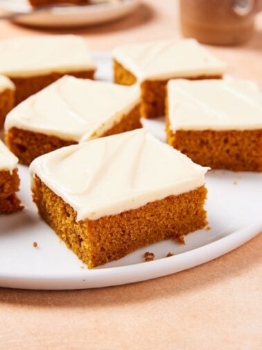 White circular plate with slices of pumpkin bars with cream cheese frosting with plate in background.