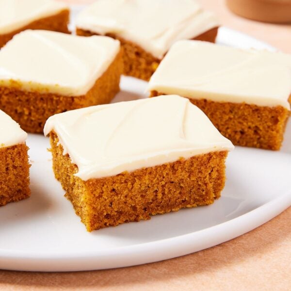 Squares of pumpkin bars with cream cheese frosting all over the top sitting on round white plate.