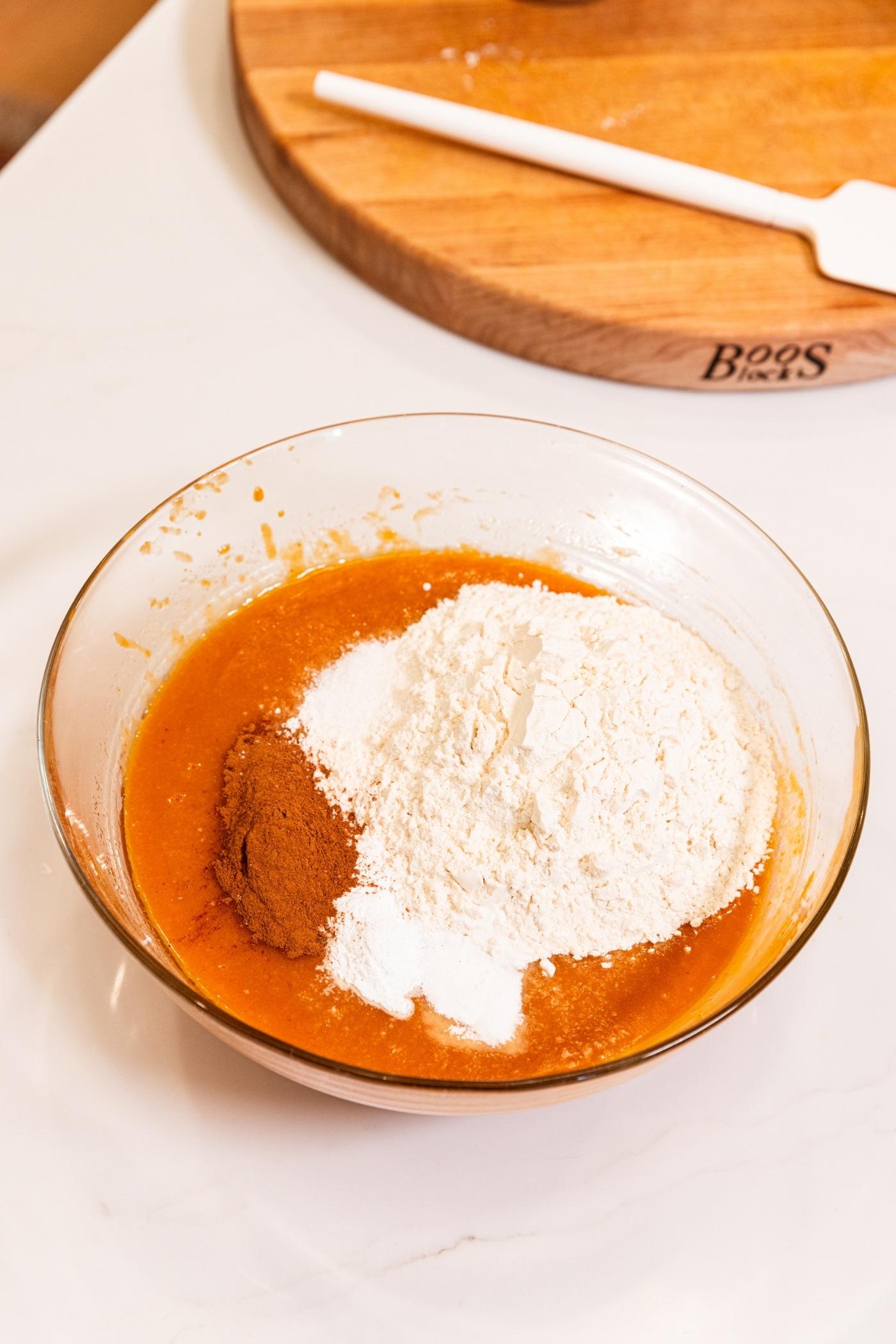 Large glass bowl with wet ingredients underneath with flour and spices poured on top before being mixed together.