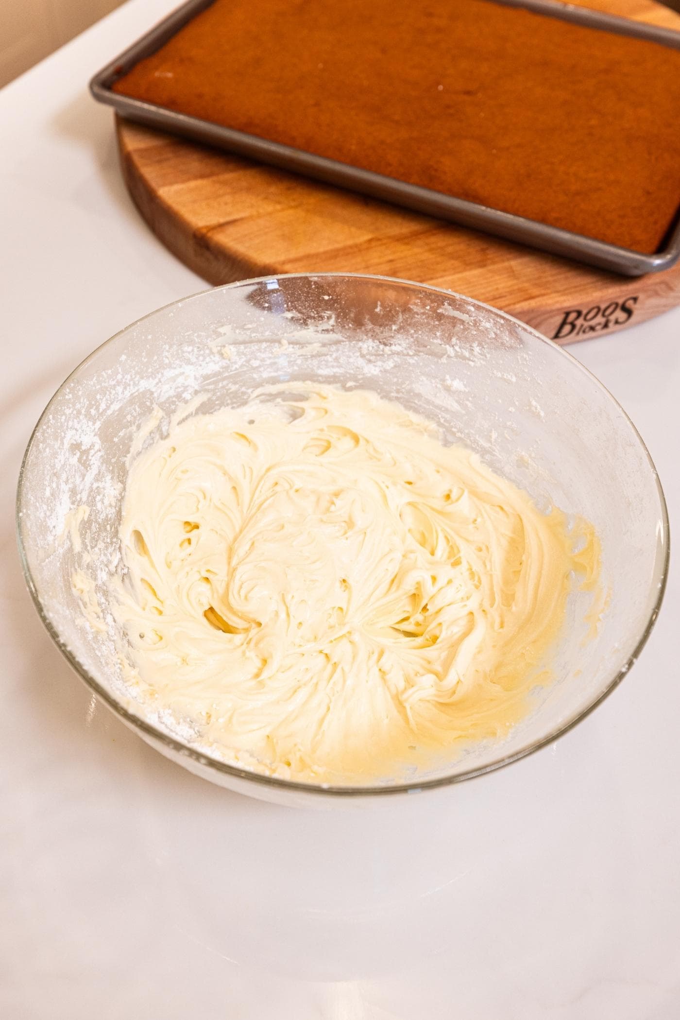 Glass bowl filled with mixed cream cheese frosting resting on white surface.